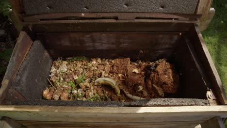 wooden composting bin opened and organic food waste dumped inside, slow motion