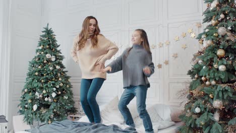 feliz madre e hija saltando arriba y abajo en la cama en una casa de lujo.