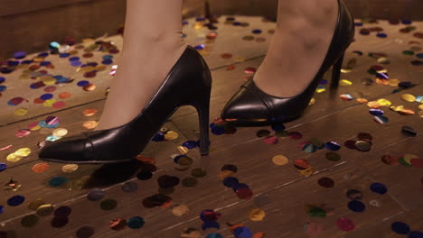 camera focuses on the black heels of a woman who is standing on the floor full of confetti at the new year's party