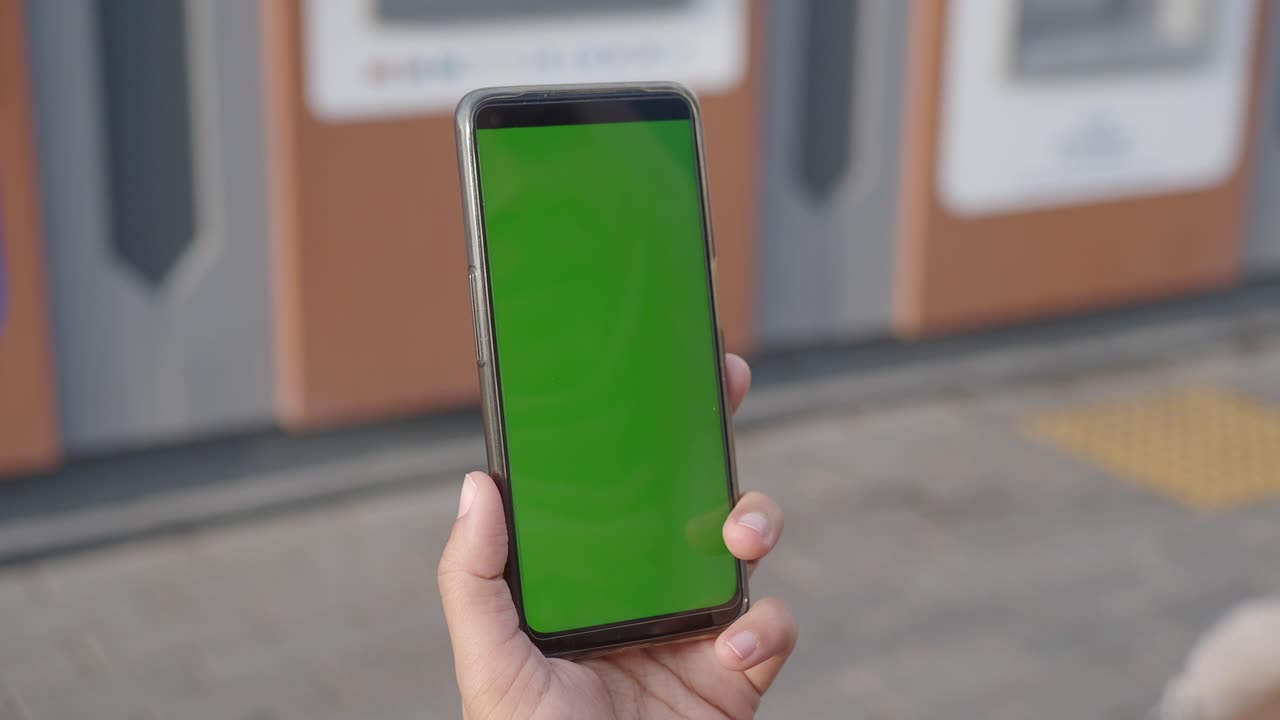 Persona che tiene in mano uno smartphone con schermo verde all'aperto