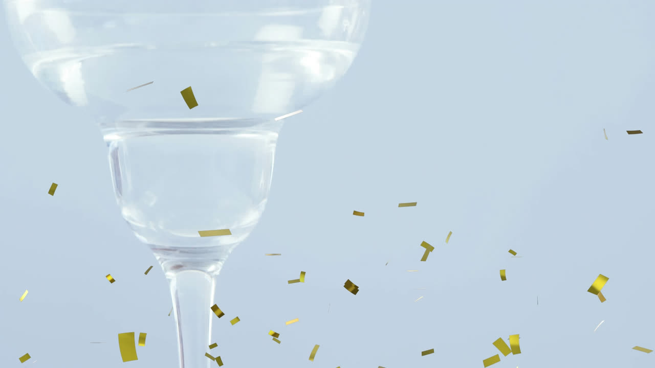 골든 콘페티가 올리브 위로 떨어지고 회색 배경에  ⁇ 테일 잔으로 떨어집니다.
