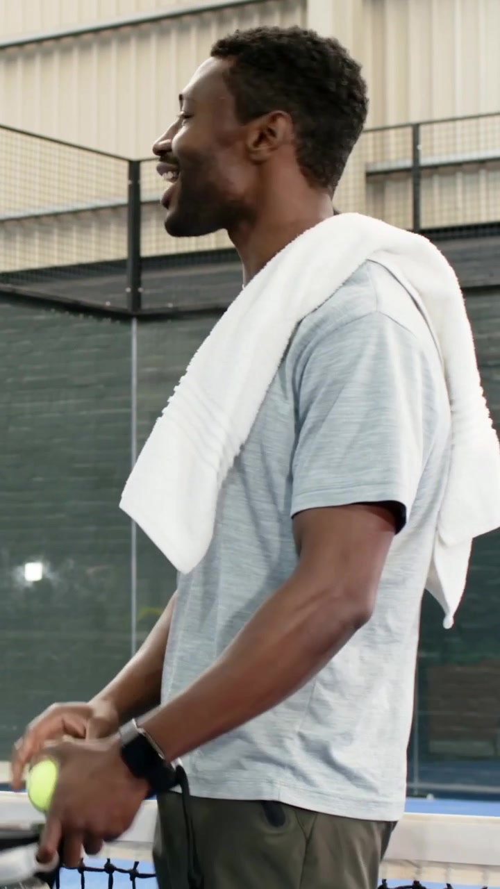 Vertical video: Reaching player picking up yellow ball at padel net, adjusting towel, copy space