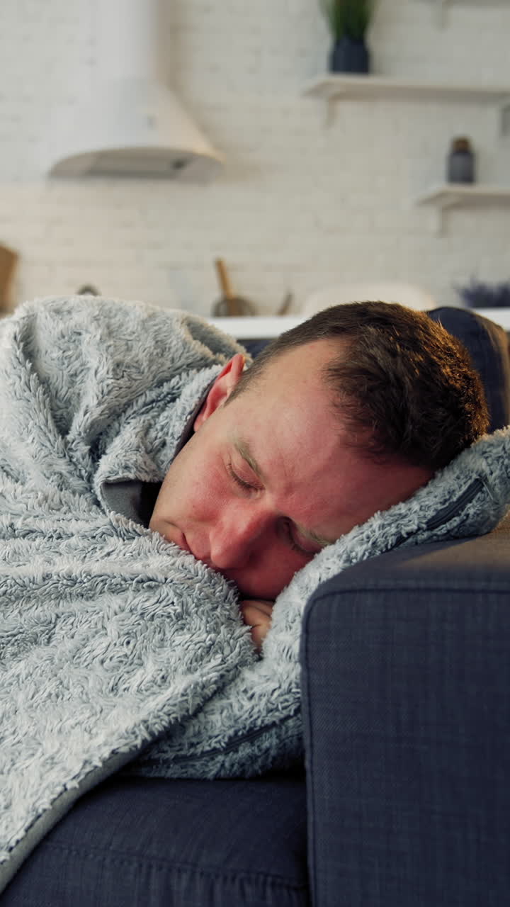 Sick man under warm blanket on comfortable couch at home. Pandemic. Quarantine concept. Vertical video