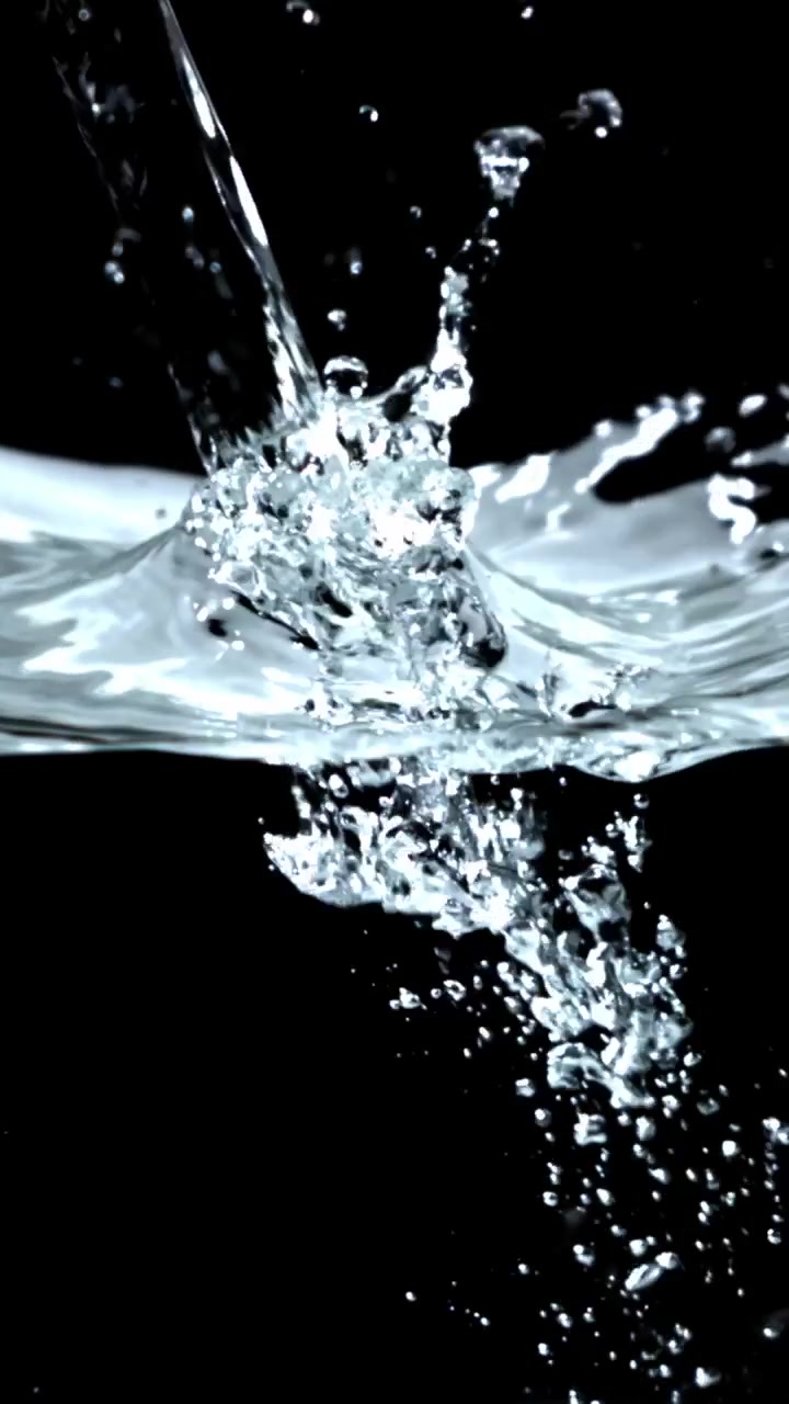 Movimento rallentato di acqua limpida che si versa e schizza su sfondo nero.