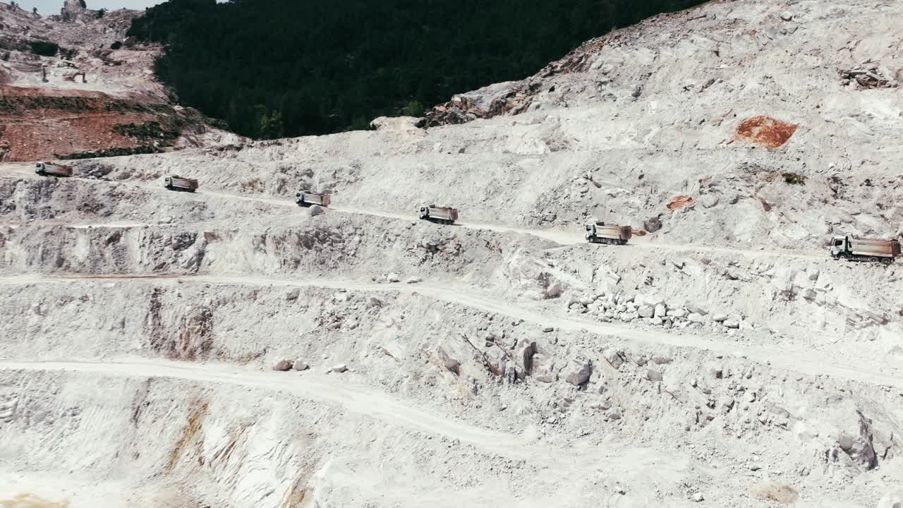 Terraced quarry with trucks navigating excavation paths, captured in stunning aerial footage.