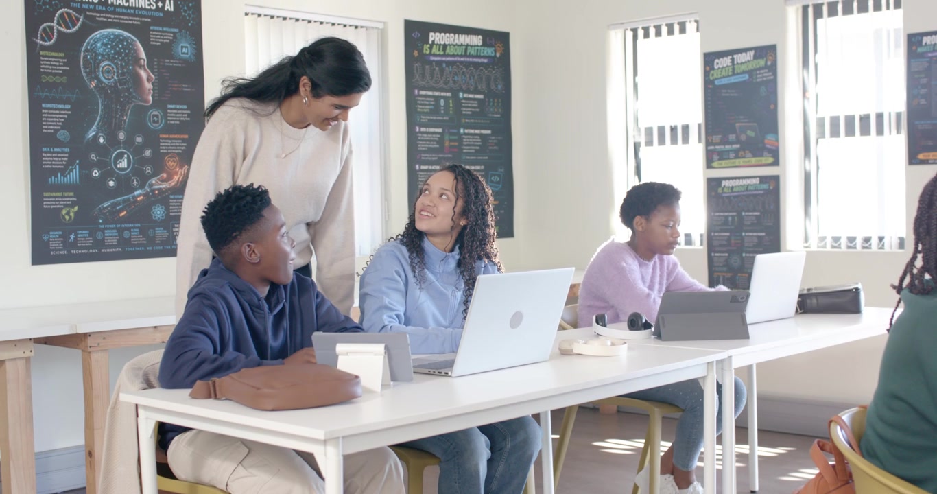 Studenti adolescenti afroamericani e insegnante indiano che entrano in laboratorio, chinati su un laptop per guidare la programmazione
