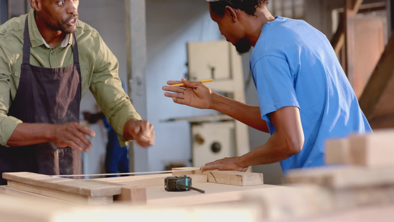 Measuring planks African American coworkers working at carpentry workshop with pencil and glasses