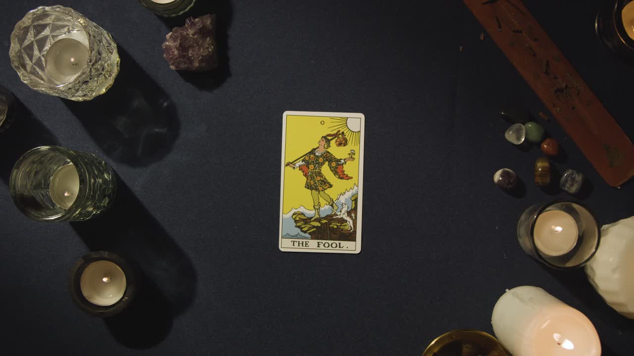 toma aérea de una persona que da una lectura de cartas del tarot colocando la carta del tonto en la mesa