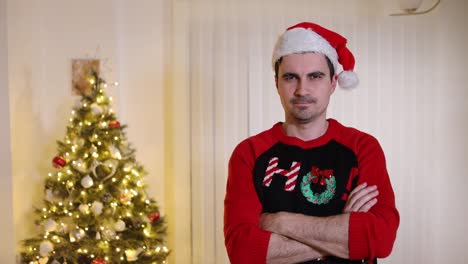 mad-looking man in santa hat and christmas sweatshirt standing with arms crossed on his chest