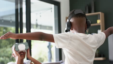 Happy-african-american-brother-and-sister-in-vr-headsets-playing-on-sofa,-slow-motion