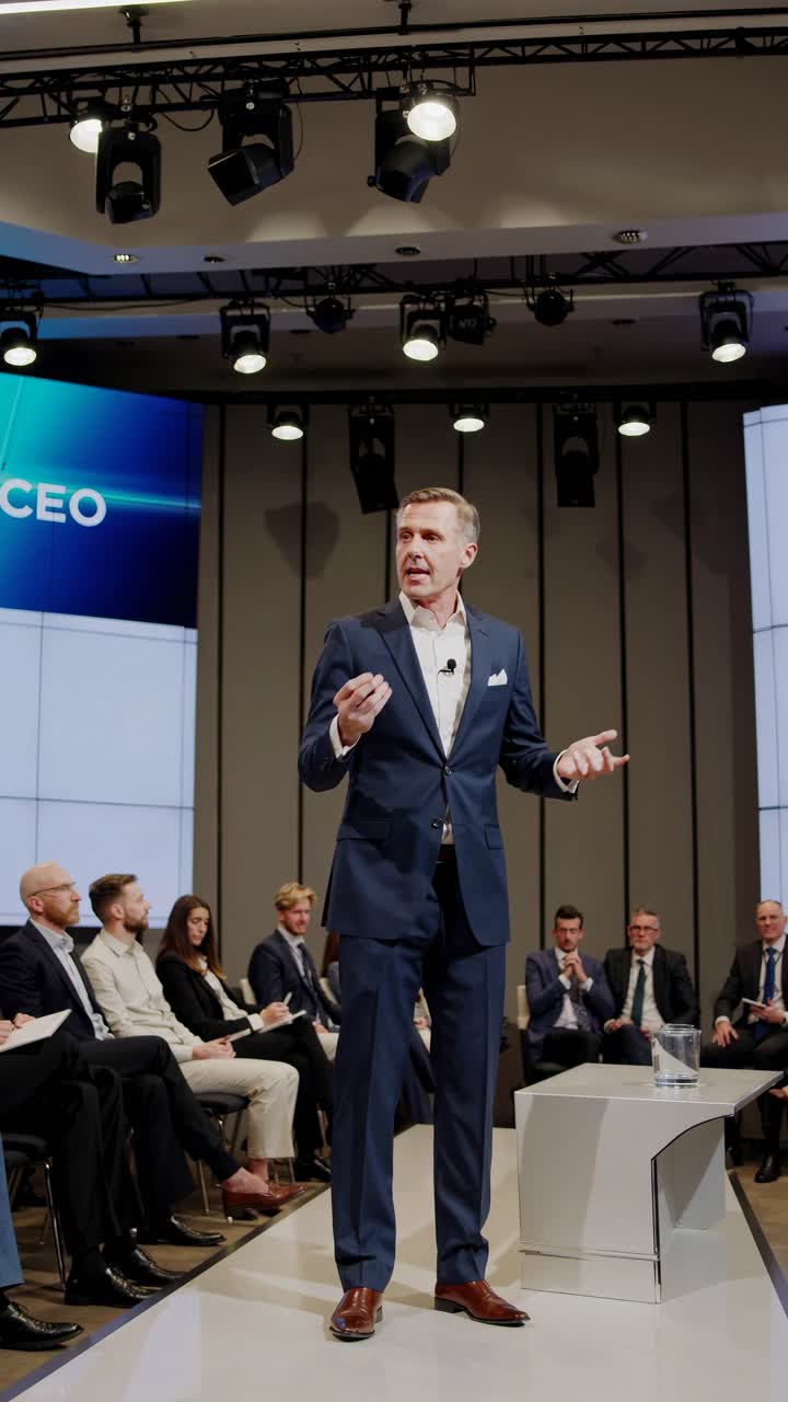 A dynamic low-angle video captures a confident speaker in a suit addressing an audience in a modern
