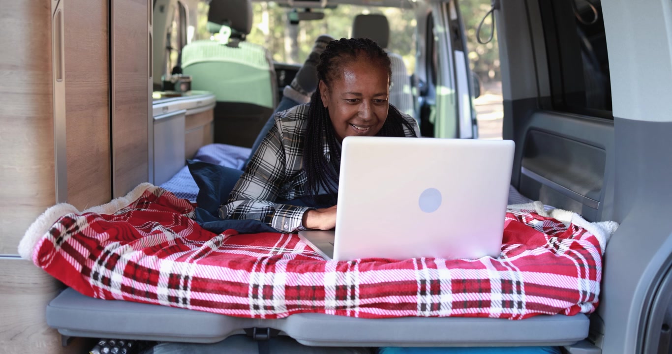 Donna felice che usa il laptop mentre è sdraiata in camper