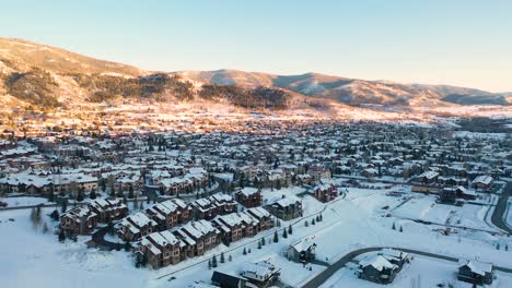 snow-covered roofs of ski lodges and houses in steamboat springs, colorado with stunning mountain range in background. wide aerial drone