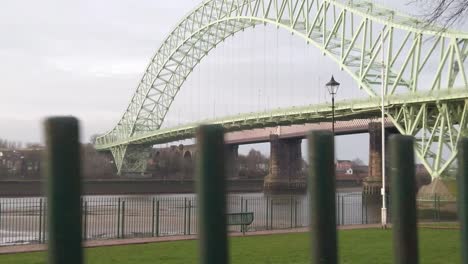 Runcorn-Silver-Jubilee-Bridge-Parallaxe-Hinter-Vorbeiziehenden-Parkgeländern-Aus-Eisen---Waterfront-Victoria-Promenade-Baum-Grünfläche