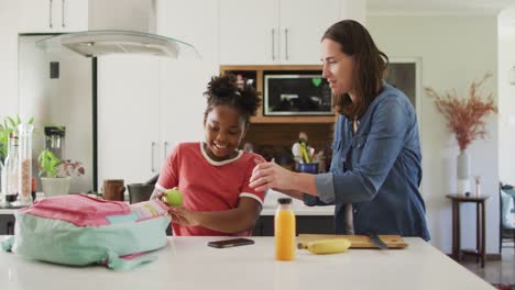 happy caucasian woman and her african american daughter packing food together
