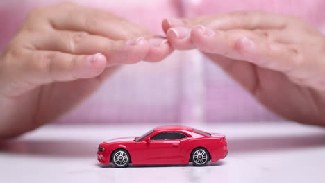 close-up shot of hands hovering over a small toy red sportscar, manifesting a desire to own a new vehicle