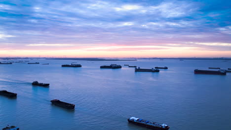 sunrise dry cargo vessels ships anchored waiting for port entrance to loading in industrial port, reflecting slowdown in freight traffic, backlog of ships wait to unload due to imposed trade barriers
