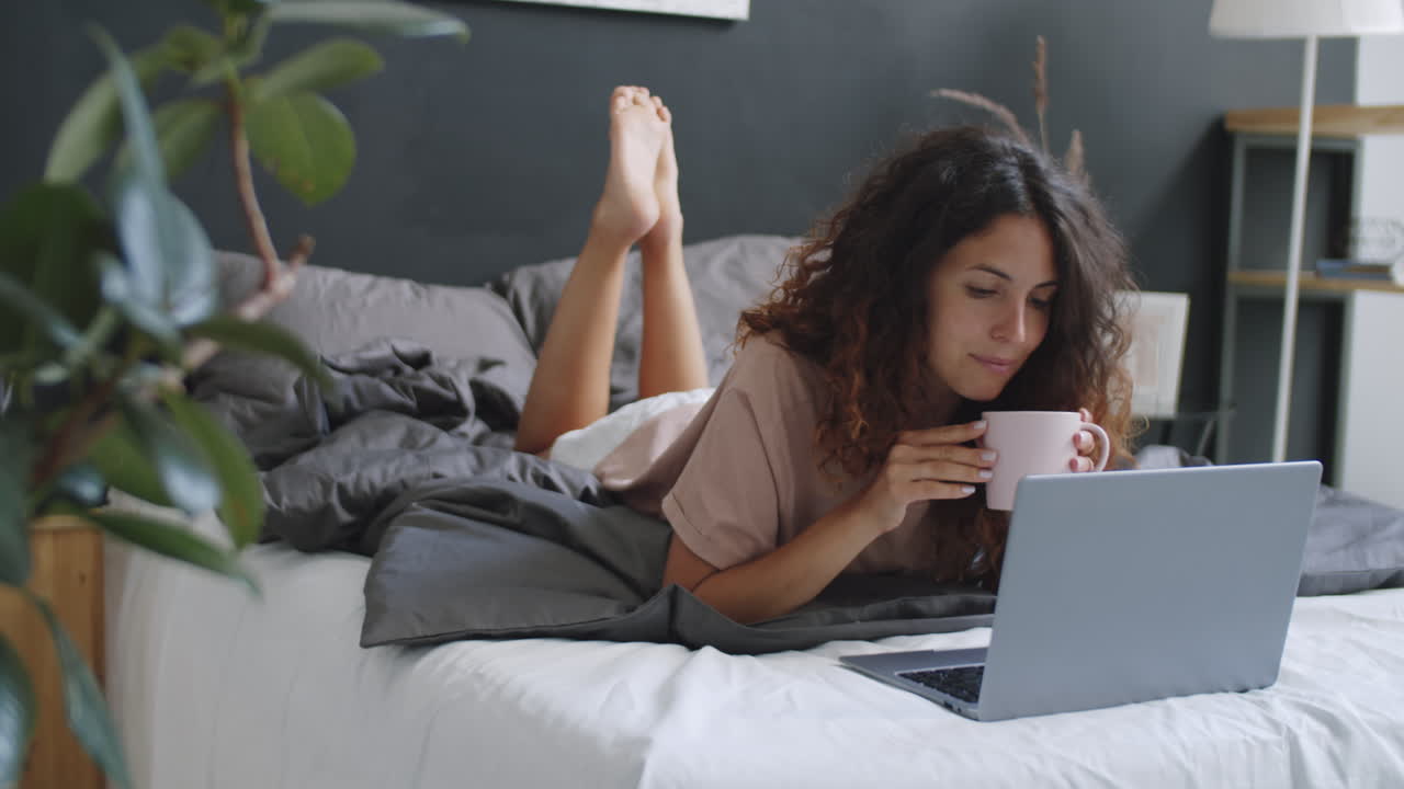 Woman relaxing on bed with laptop and coffee