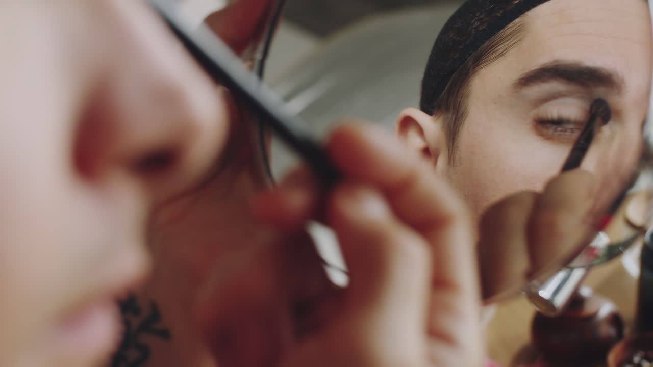 hombre transgénero aplicando sombra de ojos y mirándose en el espejo