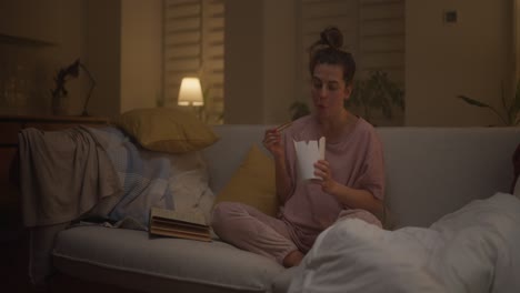 woman eating noodles on the couch at night