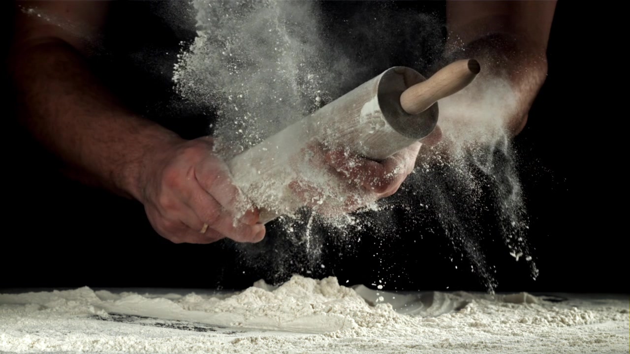 Chefshanden tikken op de deegroller, stuivende bloem in slow motion