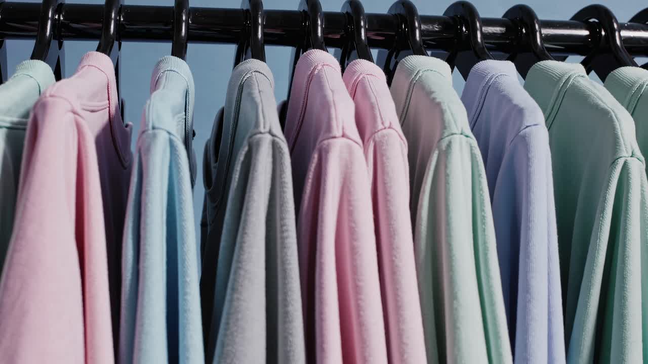 A row of pastel shirts on hangers, captured from a low-angle. The video style emphasizes soft colors