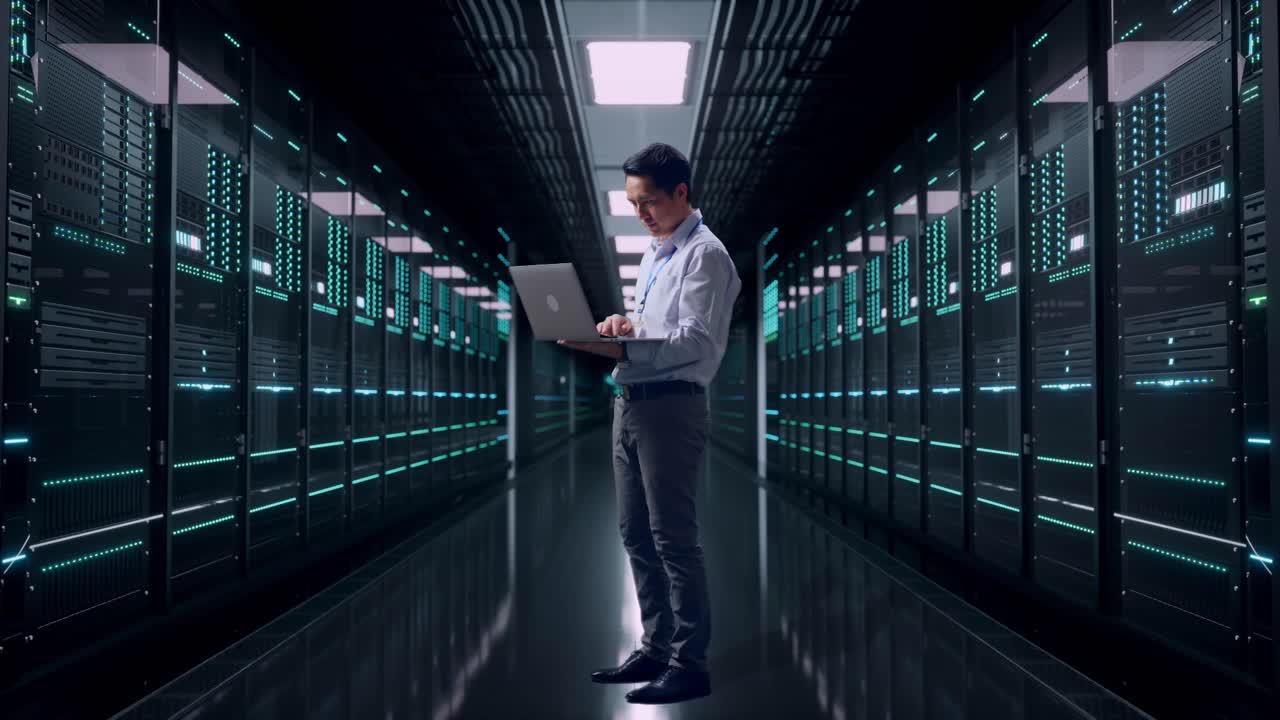 Full Body Side View Of An Asian Male Professional Worker Standing With His Laptop in Server Room Data Center, Typing On His Laptop'S Keybaord With Meditation