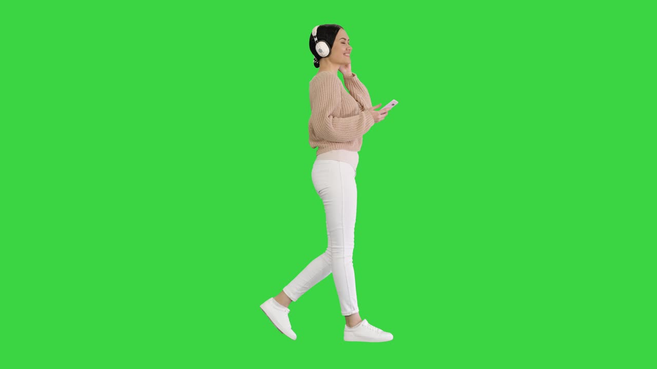 행복한 소녀가 걸어가며 스마트 폰으로 음악을 듣고 녹색 화면에 헤드폰을 착용하고, 초록 화면에 크로마 키를 착용합니다.