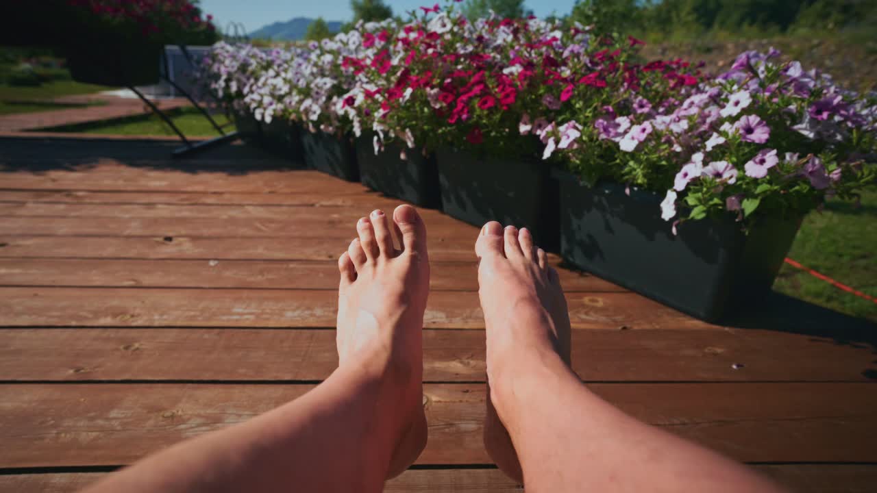 Piedi che si rilassano su una terrazza in legno con fiori colorati