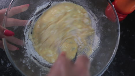 Top-down-view-of-woman-whisking-eggs-and-flour-in-a-glass-bowl