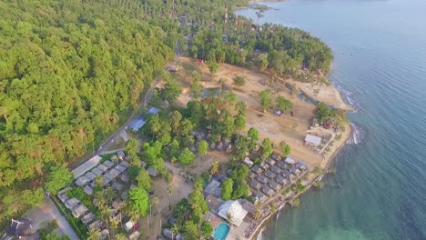 Tropical-Island-drone-dolly-shot-of-a-tourist-village-in-Thailand-with-land-cleared-for-development-with-lush-green-rain-forest-and-tropical-palm-trees-with-white-sand-beach-and-rocky-coastline