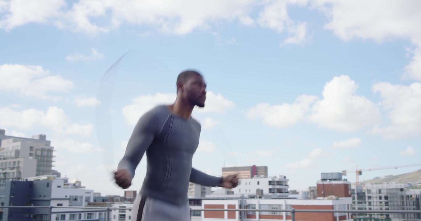 Mid-adult African man swinging rope and jumping for cardio on rooftop, wearing gray top, smartwatch
