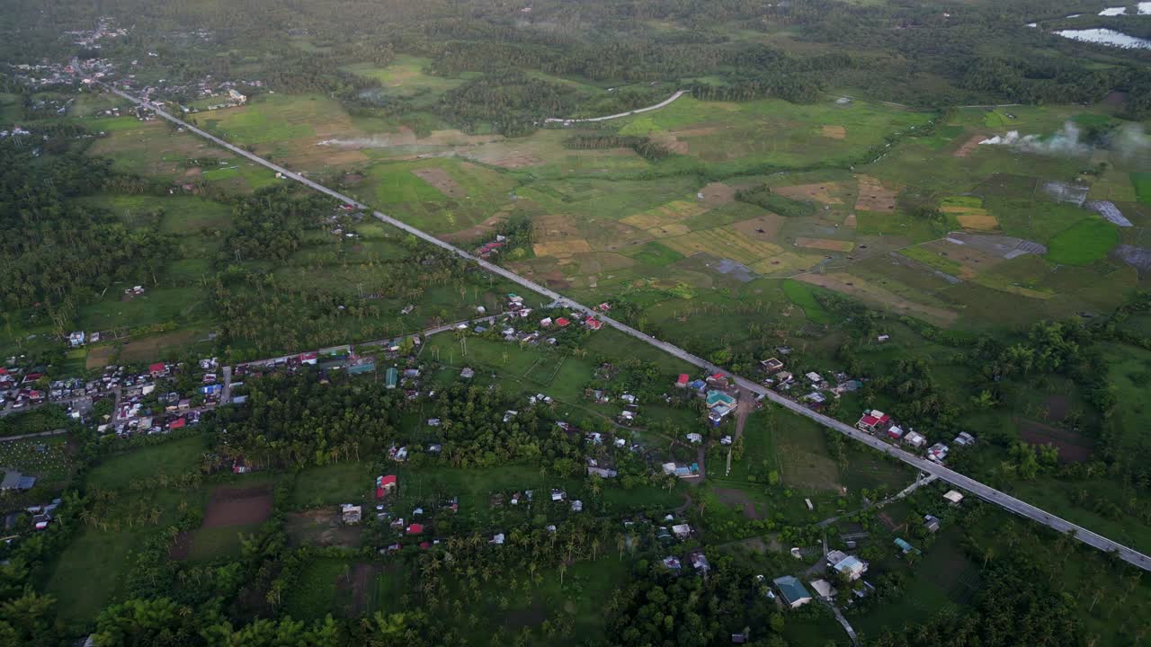 Panoramic aerial flyover shot of provincial highway road between lush farmland and barangay towns at San Andres, Catanduanes, Philippines.