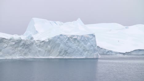 cámara lenta de icebergs flotando en el océano frente a la costa de groenlandia en un día nublado con gaviotas volando alrededor