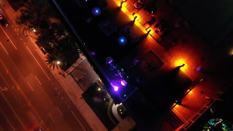 nighttime aerial top-down bird's eye pedistal movement of rooftop bar and street with walking people and passing cars