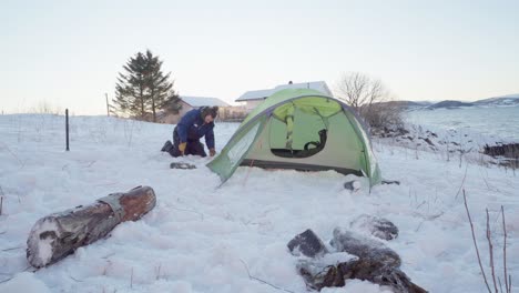 camper putting stake on corner of camping tent at winter