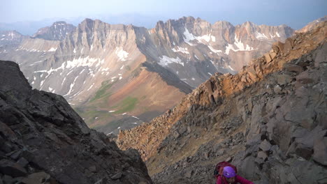 Female-Climber-on-High-Steep-Rocky-Hill-With-Scenic-Sunny-Valley-in-Background