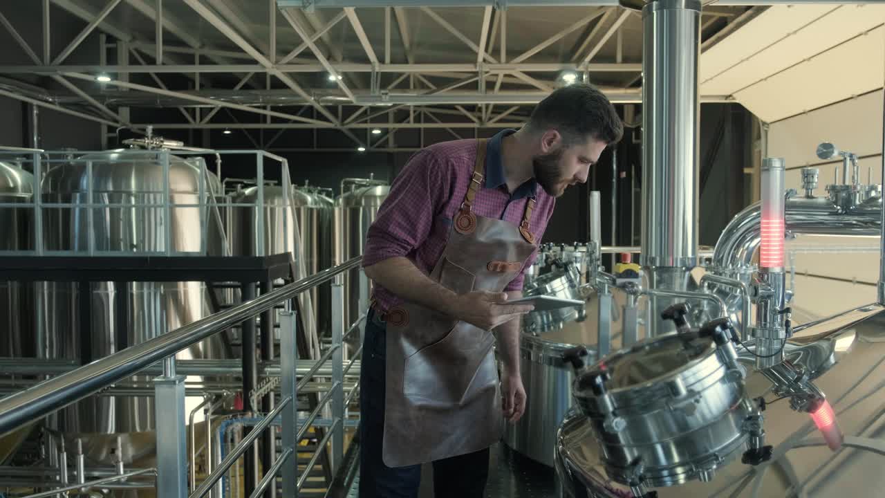 un joven cervecero con un delantal de cuero supervisa el proceso de fermentación de la cerveza en una fábrica de cerveza moderna