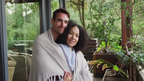 smiling mixed race couple wrapped in sheets embracing each other in the balcony at vacation home