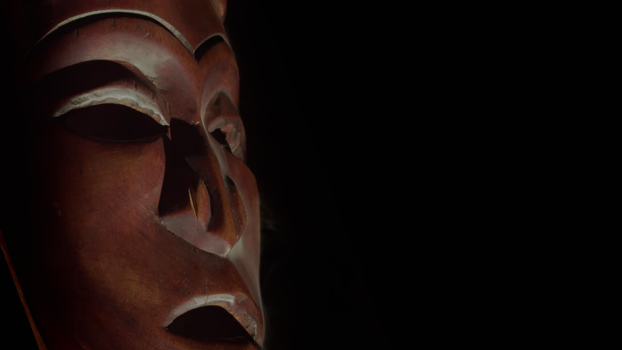 Close-up Topeng Afrika Ukiran dengan Asap Mengepul di Latar Belakang Hitam dan Ruang Teks di Kanan. Ideal untuk Tema Dokumenter, Pameran, dan Warisan Budaya.