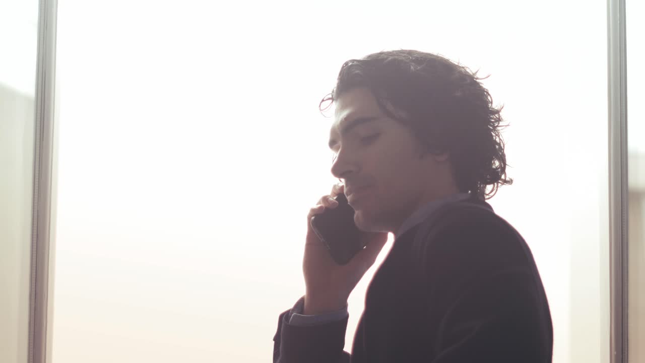 Giovane uomo che parla al telefono vicino alla finestra in una luce soffusa