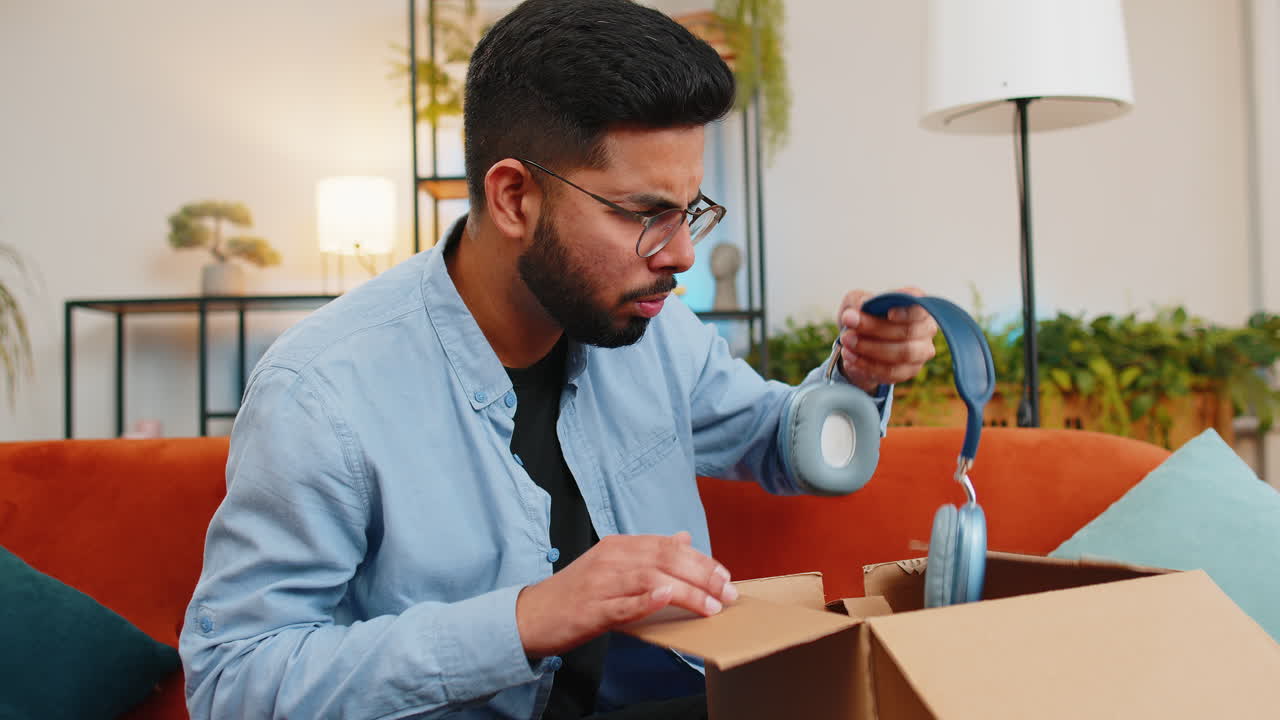 Dissatisfied Indian man customer open cardboard box receive damaged broken wireless headphones