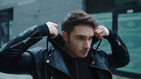 portrait of young man walking street. handsome man correcting hood