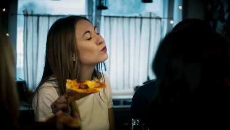 joven hermosa chica caucásica comiendo pizza con amigos en una mesa de bar de la cocina en una fiesta de casa de diversión casual con bebidas