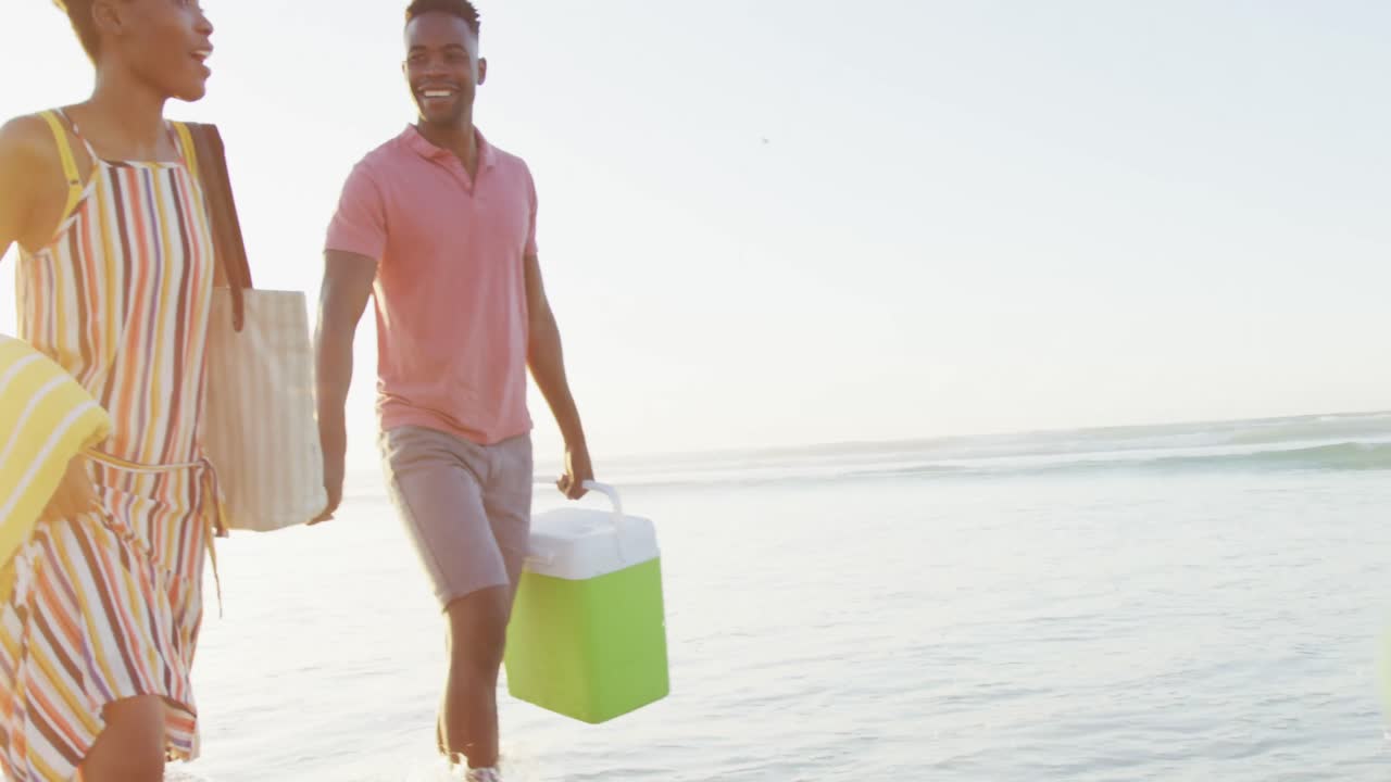 Happy african american couple walking with daughter and son on sunny beach