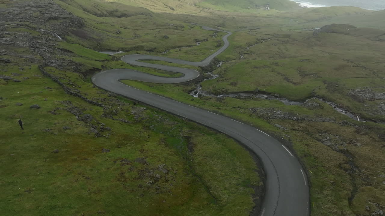 Scenic aerial shot flying over a curvy road through the green mountains of Faroe Islands, Denmark