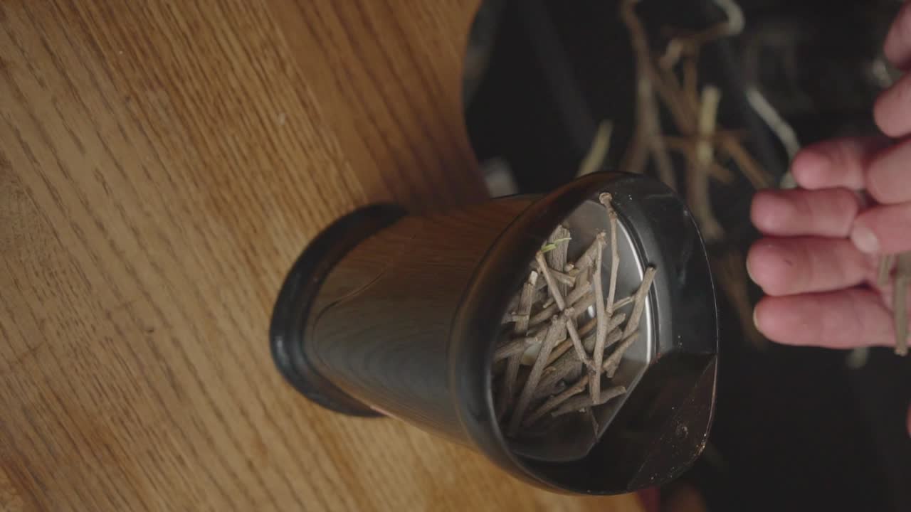 manos poniendo pedazos de ramas de clementino en la licuadora, triturando en forma de polvo