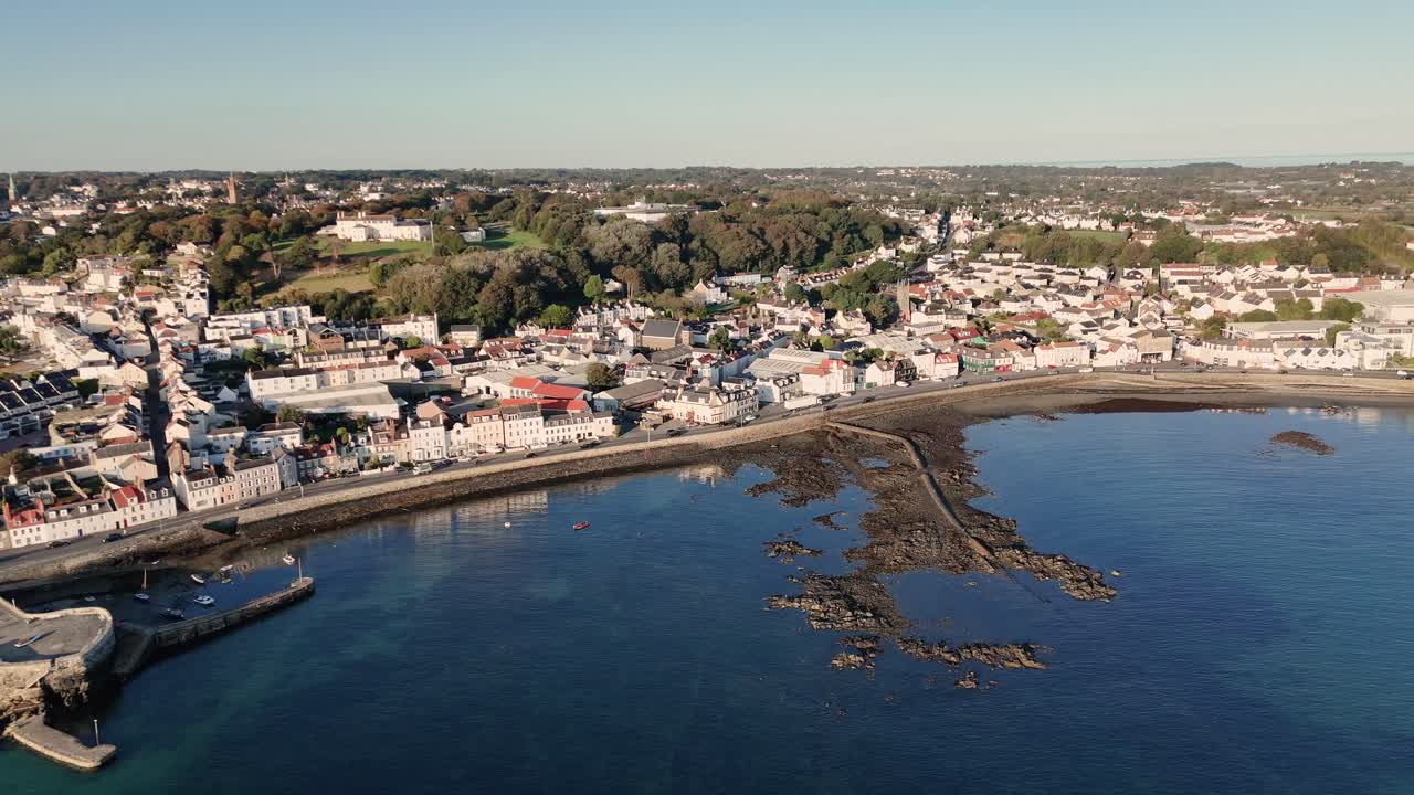 Guernsey.Belle Greve Bay high drone footage along the sea front from Salerie Corner to the Longstore with calm clear water on sunny day with views across the Island