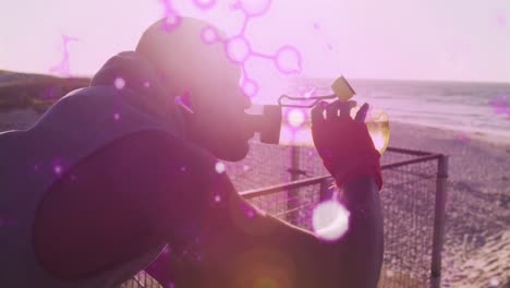 Glowing-molecular-structures-floating-against-african-american-fit-man-drinking-water-near-the-beach