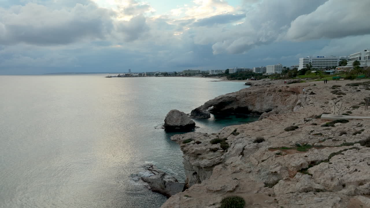 puente del amor o puente del amor en chipre al crepúsculo con un cielo dramático en el cabo greco, la costa de la ciudad de ayia napa en el fondo - retirada aérea hacia el borde del acantilado